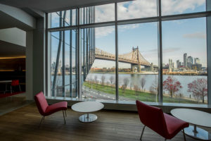 Chairs and end tables facing a wall of windows with the a bridge and city skyline.