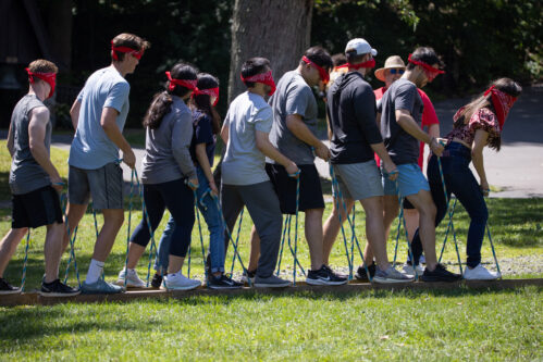 Group of students blind folded standing on two boards holding ropes.