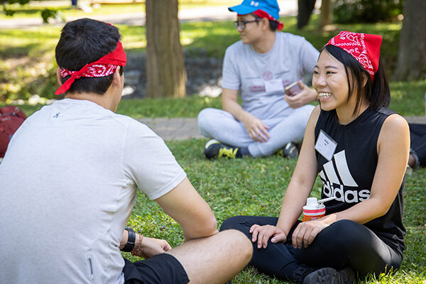 Two people sitting cross-legged on grass with red bandanas on their heads.