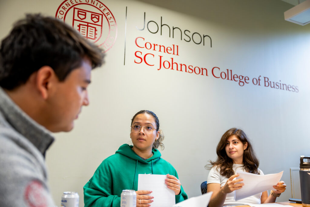 Three people holding papers in front of a Johnson branded wall.
