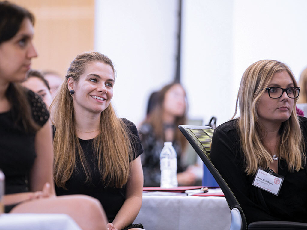 Three women sit in a classroom listening to a speaker.