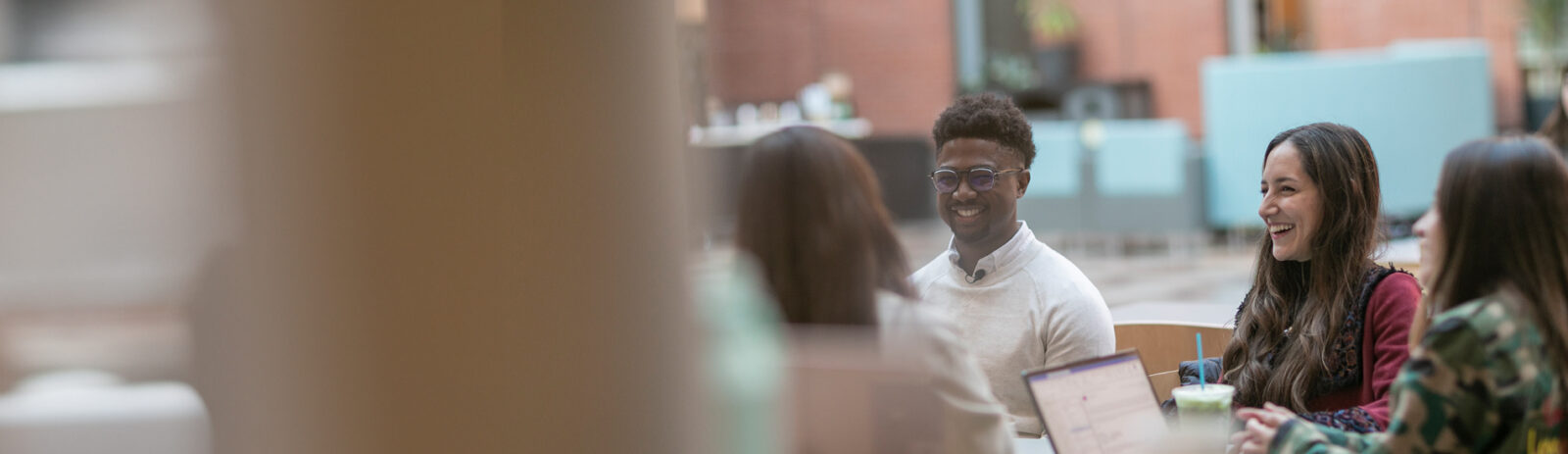 A group of students sitting at a table talking in the Dyson Atrium in Sage Hall.