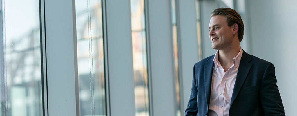 A man in a suit smiles as he looks out a wall of windows.