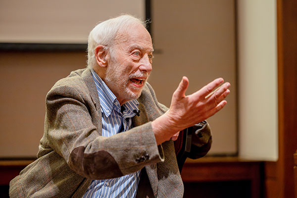 John Marks leaning forward in his chair and gesturing with both hands in the air; his facial expression shows he is passionate about what he is saying.