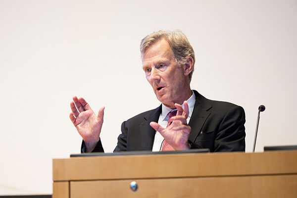 Peter Nolan standing behind a podium and speaking as he gestures with his hands.