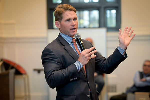 A man in front of a lecture hall speaking ino a microphone and gesturing.