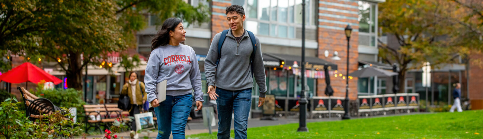 A young woman and young man walk and talk together in a grassy plaza on Roosevelt Island in NYC