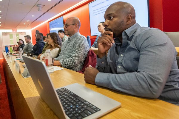 Students sit in a tiered classroom with laptops open in front of them.