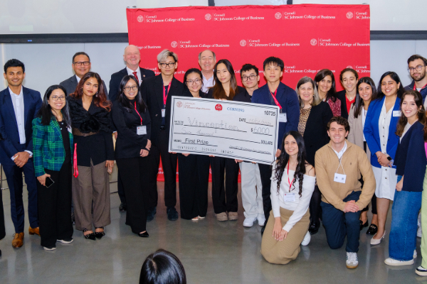 Winners of the competition holding a large check, surrounded by other participants. Organizers and funders are standing behind them; a red Cornell banner appears in the background.