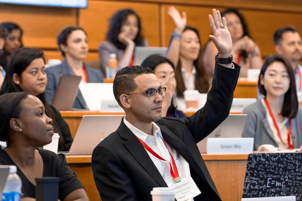 A professional raising his hand in an MBA boardroom, surrounded by diverse peers, showing the balance of working full time and getting a masters degree.