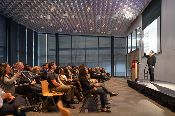 A man speaking on stage in front of a large room filled with people.