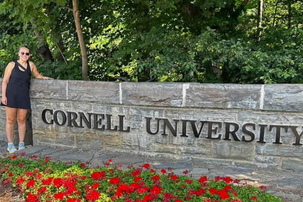 Image of Lauren Whitehead during the summer in front of the Cornell University sign on campus